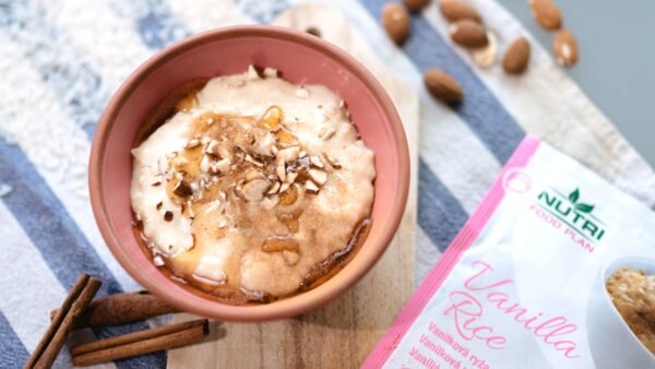 Frothy latte in a pink mug topped with cinnamon and almond flakes on a wooden board, with cinnamon sticks nearby.